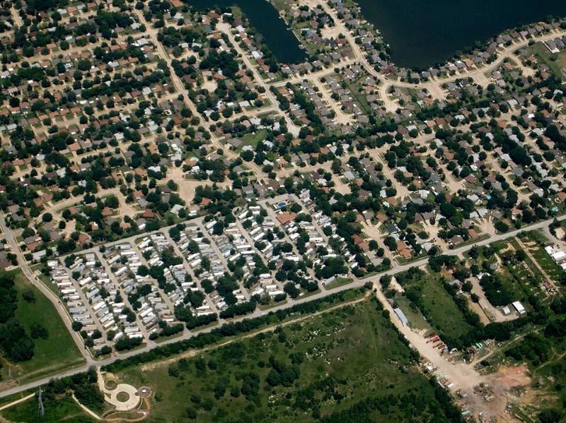 Aerial photograph showing manufactured-home rows and internal roads beside surrounding neighborhoods.