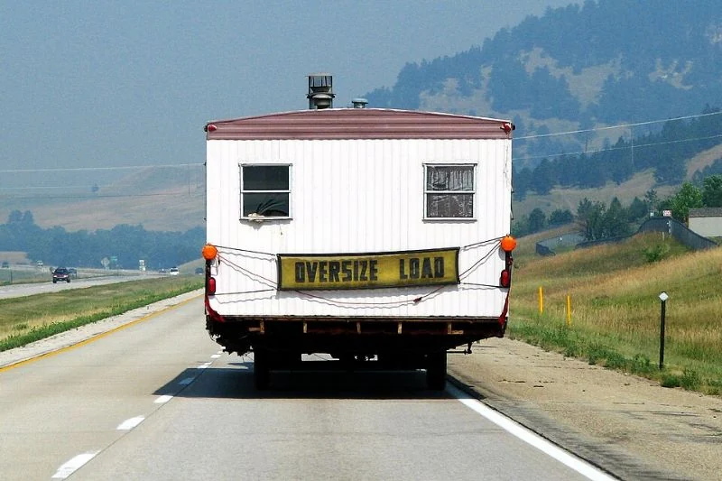 Rear view of a mobile home being transported on a highway with an oversize-load sign.