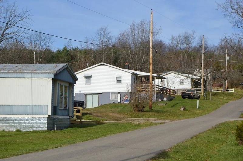 A narrow residential street beside homes, grass verges and overhead utility lines.