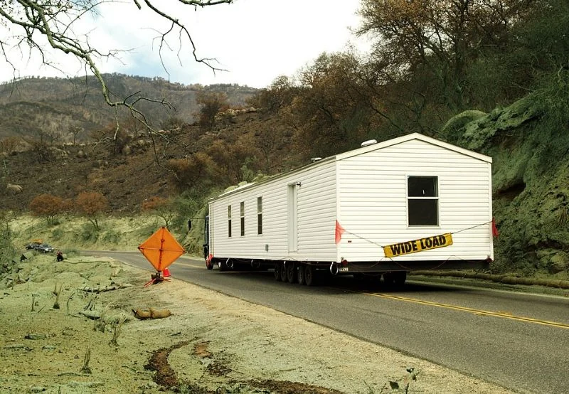 A mobile home being towed around a bend on a road through hilly terrain.